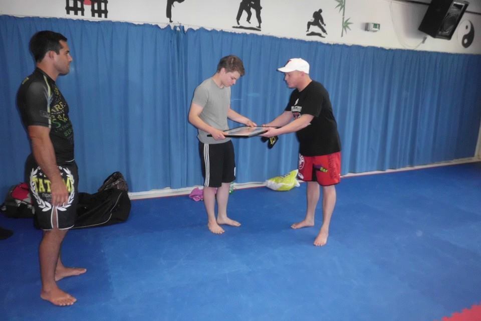 Drei M&auml;nner stehen in einem Sportraum, einer &uuml;berreicht einem anderen ein Tablet, der dritte schaut zu.