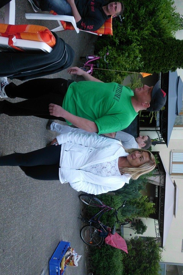 Zwei Personen unterhalten sich auf einem Gehweg, im Hintergrund einige Fahrr&auml;der und gr&uuml;ne Pflanzen.