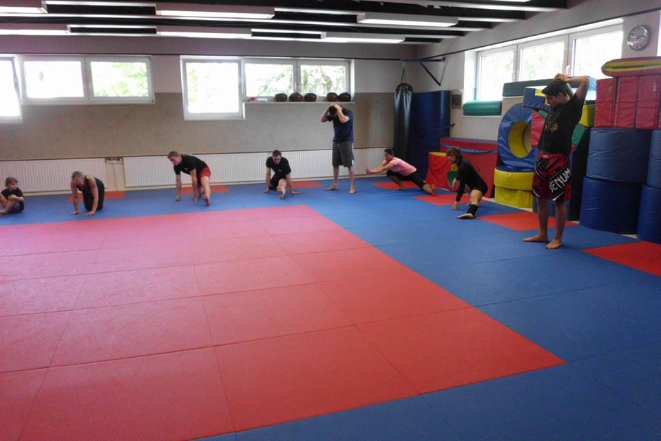 Gruppentraining im Raum mit bunten Matten, Teilnehmer beim Stretching und &Uuml;bungen auf rotem und blauem Boden.