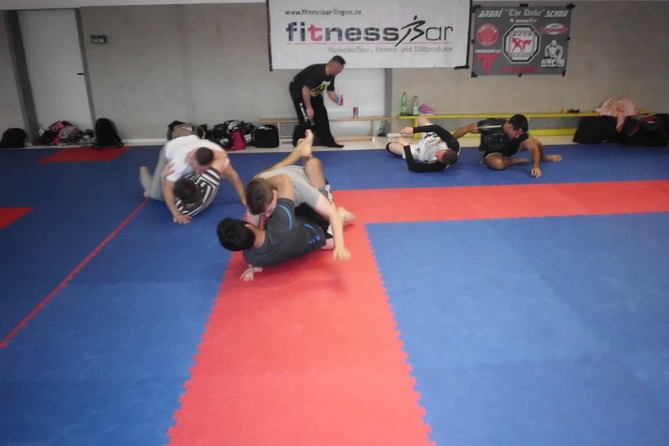 Gruppe von K&auml;mpfern trainiert auf einer blauen und roten Mattenfl&auml;che in einem Fitnessstudio.