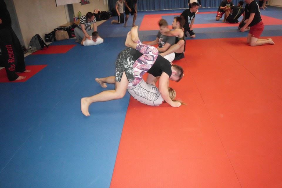 Zweikampftraining auf einer blauen und roten Matte, mit aktiven K&auml;mpfern in verschiedenen Positionen.