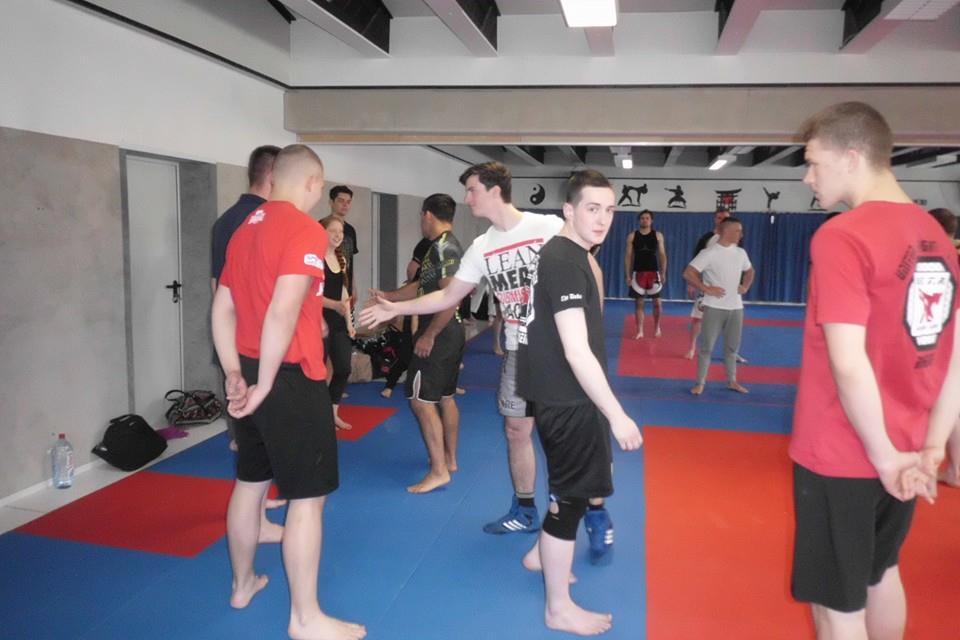 Gruppe von Kampfsportlern interagiert auf einer blauen Matte in einem Trainingsraum.