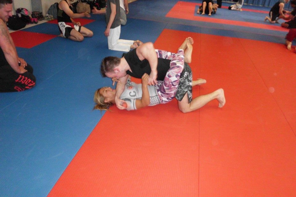 Zwei Kampfsportlertrainieren in einem Trainingsraum, einer liegt auf der Matte, der andere ist oben positioniert.