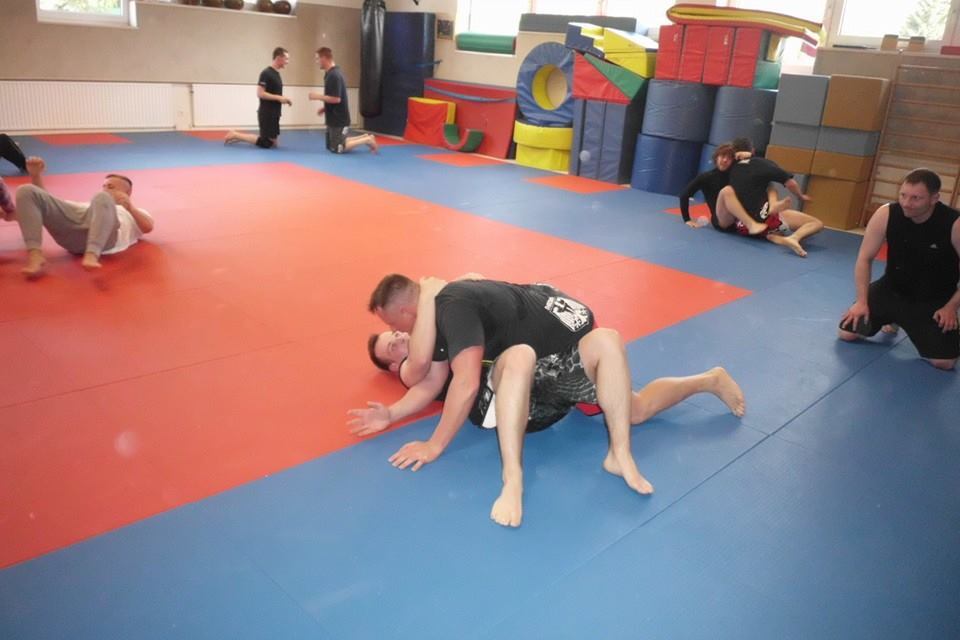 Zweikampftraining in einem Sportraum, mehrere K&auml;mpfer auf Matten in unterschiedlichen Positionen und Bewegungen.