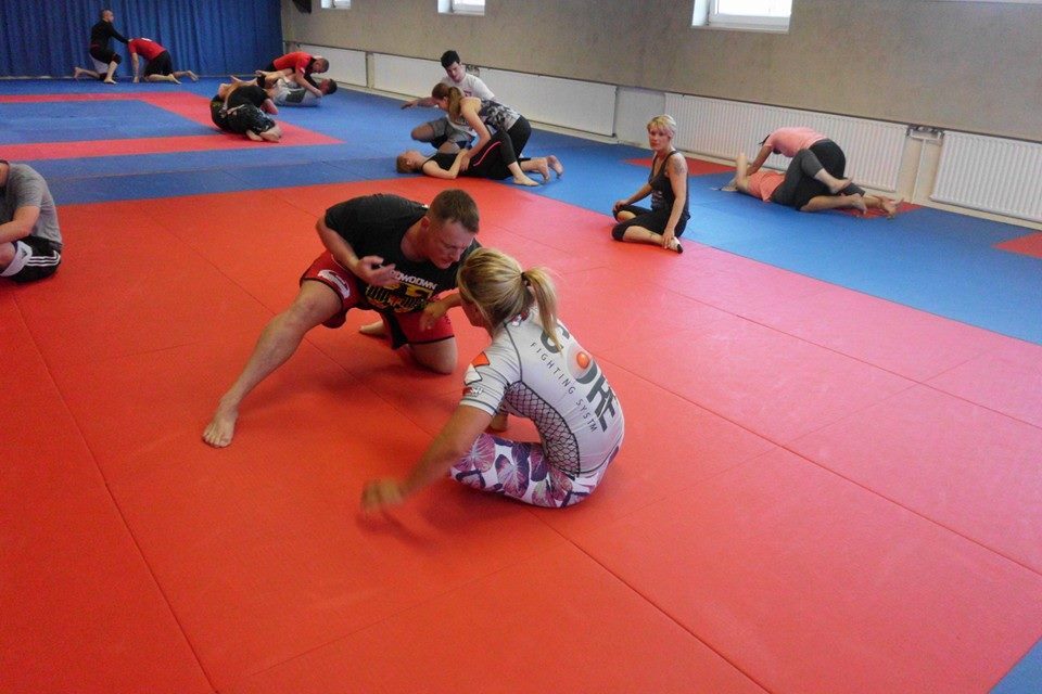 Training in einer Kampfsporthalle, mehrere Athleten &uuml;ben auf roten und blauen Matten verschiedene Techniken.