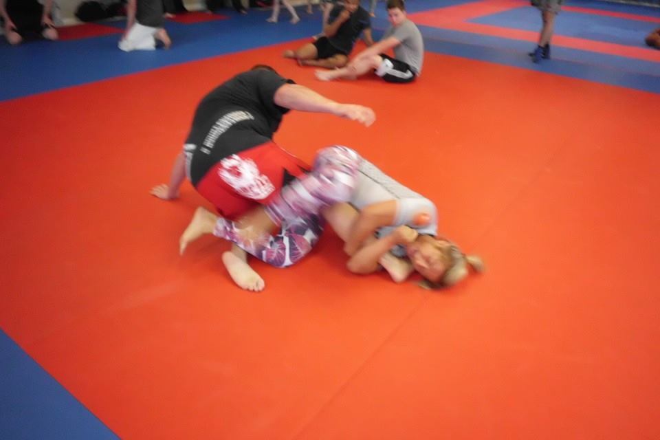Zwei K&auml;mpfer auf einer roten Matte im Grappling, einer in Schwarz und der andere in bunten Leggings.