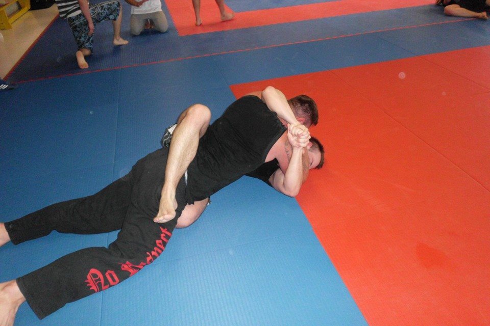 Zwei Sportler k&auml;mpfen auf einer blauen und roten Tatami, einer h&auml;lt den anderen im Griff.