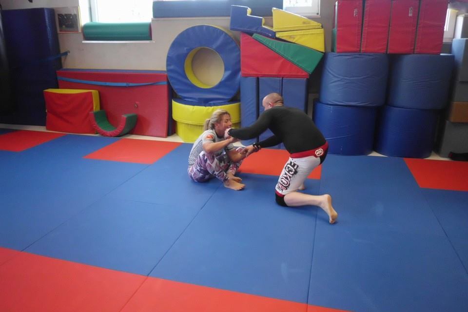 Zwei Personen in Sportbekleidung &uuml;ben auf einer blauen Mattenfl&auml;che Techniken im Kampfsport.