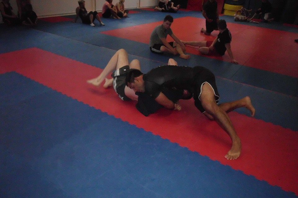 Zwei K&auml;mpfer in Sportkleidung k&auml;mpfen auf einer blauen und roten Matte in einem Kampfsporttraining.