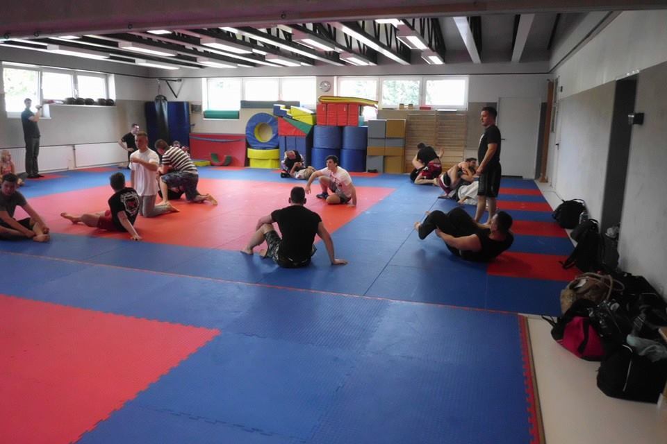 Trainingseinheit in einem Sportraum mit mehreren Personen auf einer blauen und roten Mattenfl&auml;che.