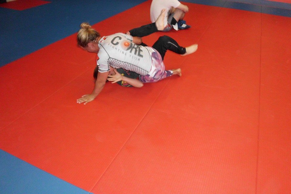 Zwei K&auml;mpfer auf einer roten Matte im engen Grappling, einer &uuml;ber dem anderen in aktiver Position.