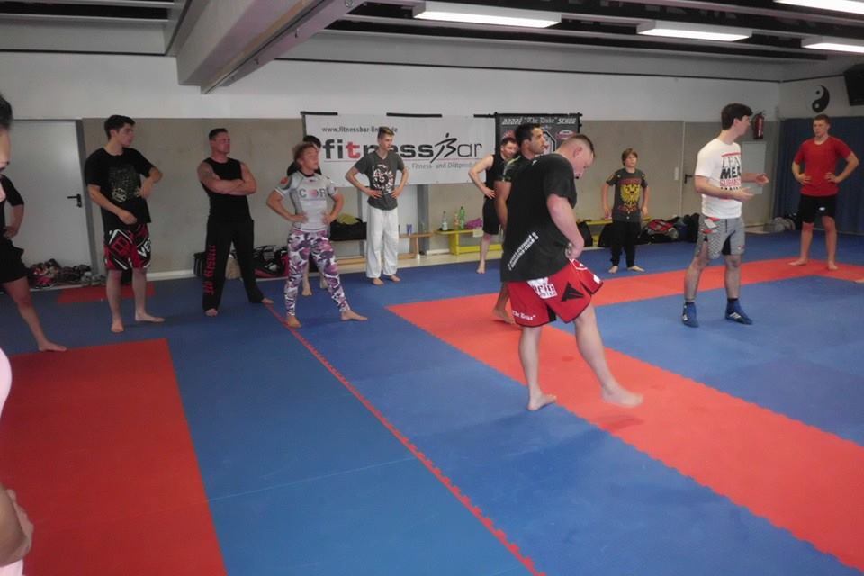 Gruppe von Kampfsportlern in Trainingskleidung in einem Dojo w&auml;hrend einer &Uuml;bung auf blauen und roten Matten.