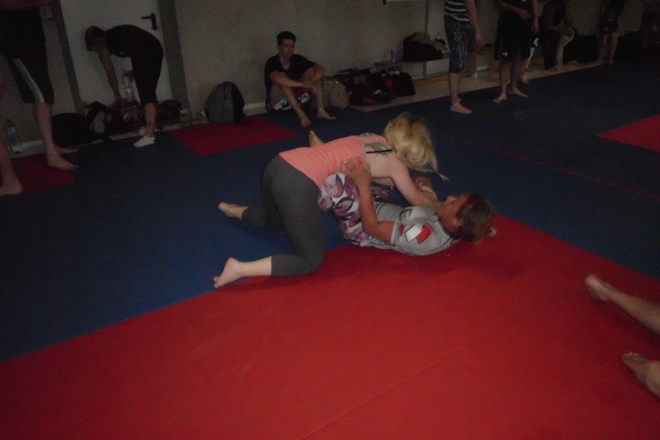 Zwei Personen k&auml;mpfen auf einer roten und blauen Matte im Training, eine Person ist oben, die andere unten.