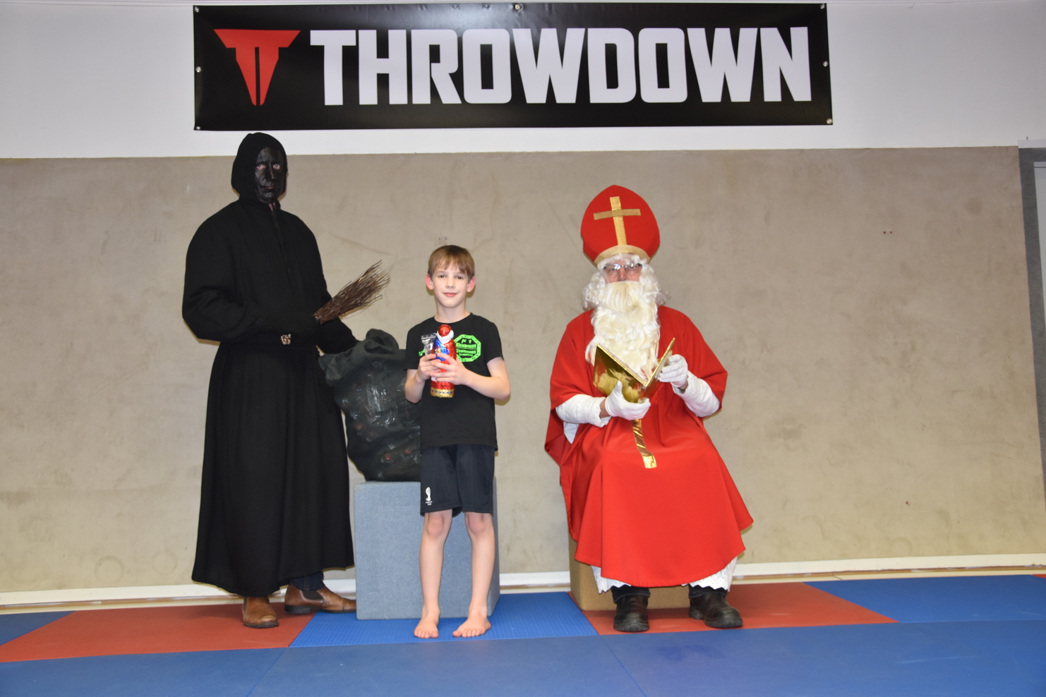 Ein Junge in Sportkleidung steht zwischen einem gruselig gekleideten Mann und einem Weihnachtsmann in rotem Gewand.