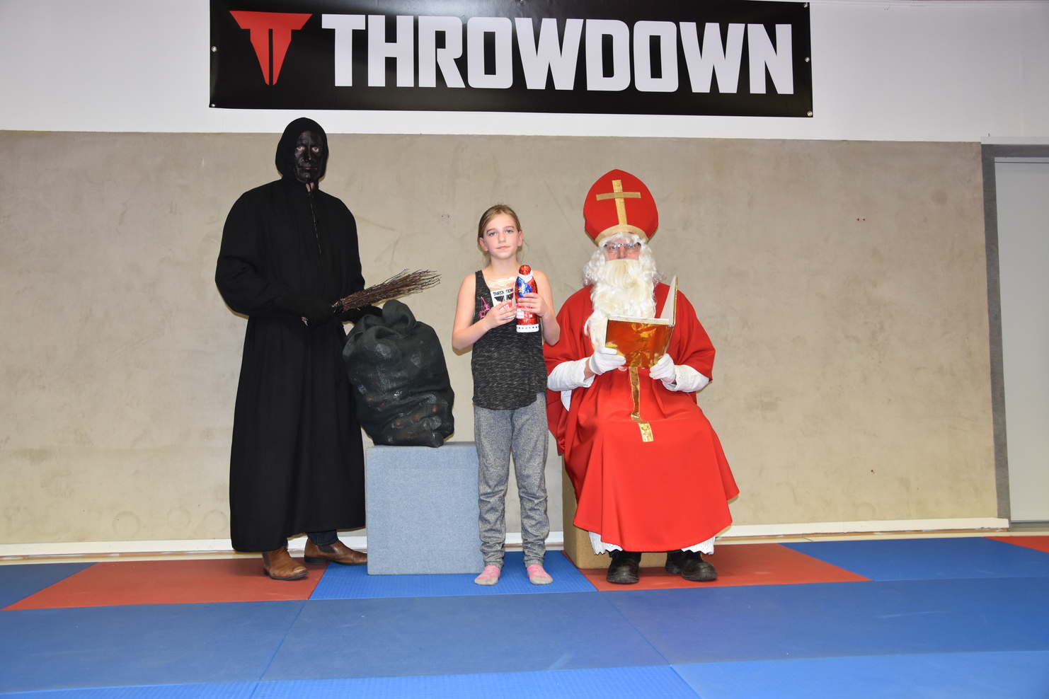 Ein M&auml;dchen steht zwischen einem schwarzen Mann in Kapuzenkleidung und einem Weihnachtsmann in rotem Gewand.