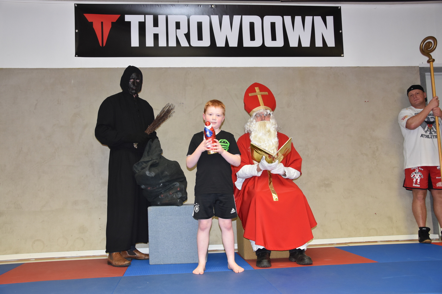 Ein kleiner Junge h&auml;lt ein Spielzeug in der Hand und steht zwischen einem bedrohlich gekleideten Mann und einem Weihnachtsmann.