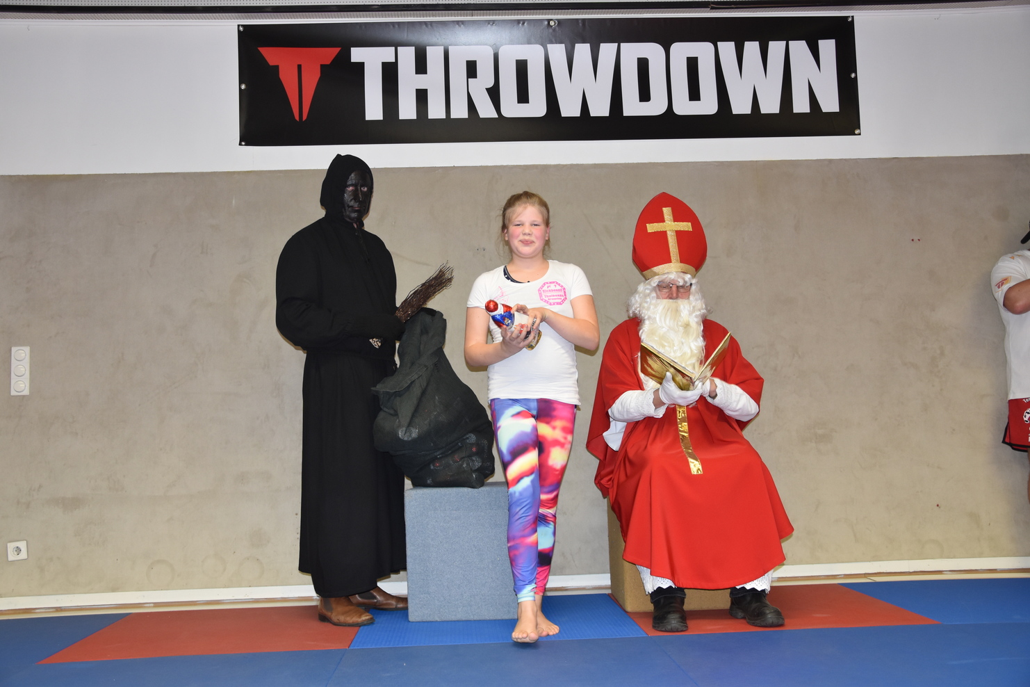 Ein M&auml;dchen mit Farbdruckleggings h&auml;lt eine Wasserpistole zwischen einer dunklen Gestalt und einem Weihnachtsmann.