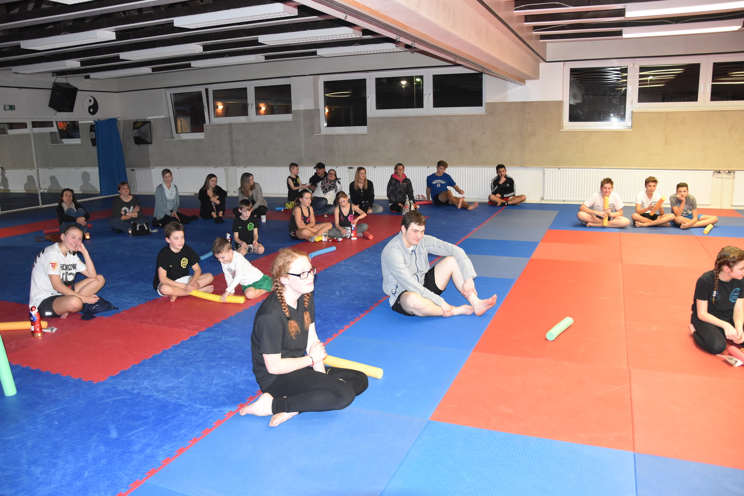 Gruppe von Sportlern sitzt auf bunten Matten in einem Trainingsraum w&auml;hrend einer &Uuml;bungseinheit.