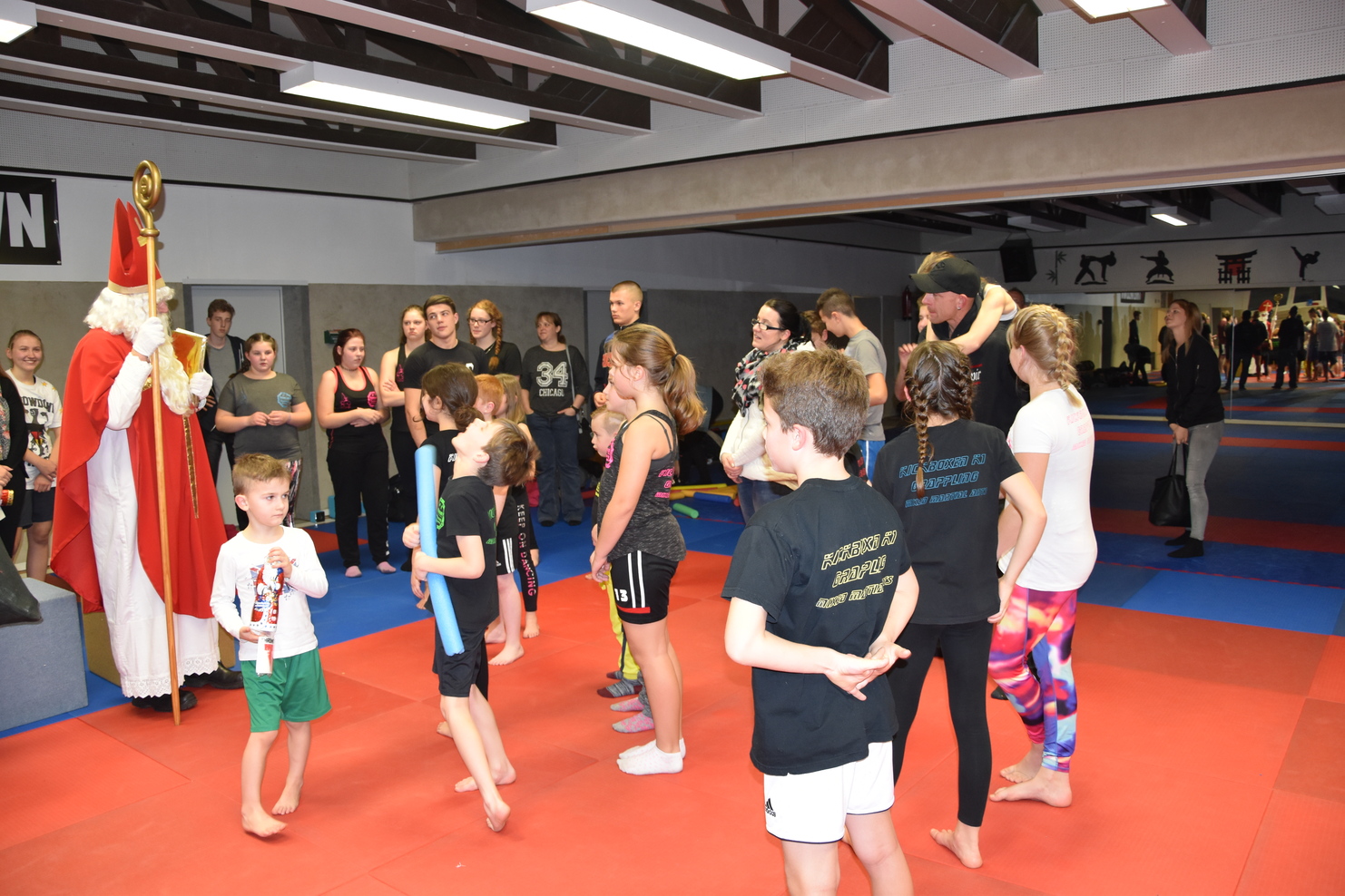 Gruppenszene in einem Kampfsportstudio mit Kindern und Erwachsenen, die einem gestiefelten Nikolaus aufmerksam zuh&ouml;ren.
