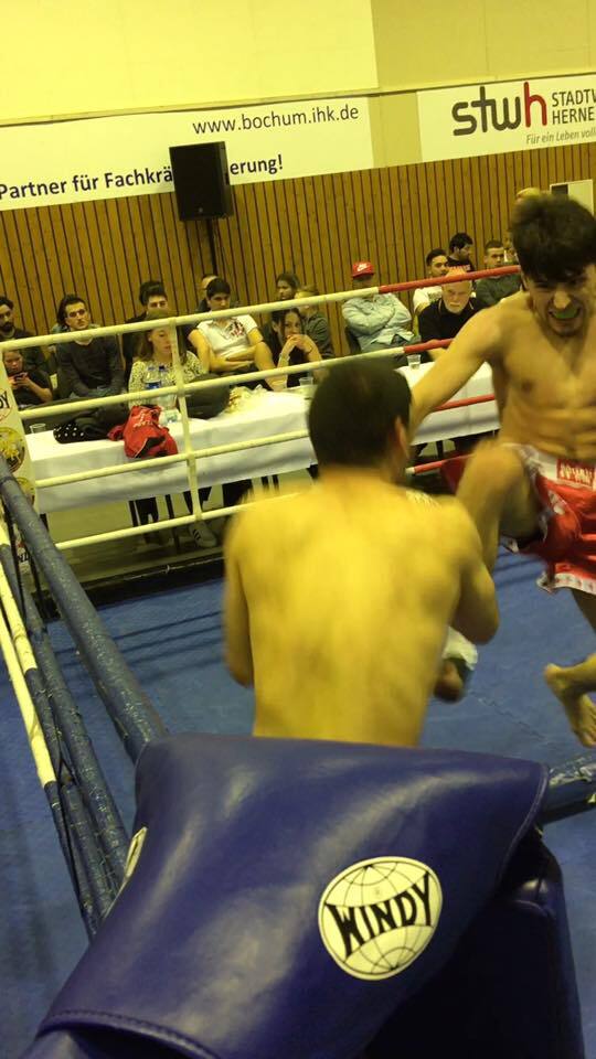 Zwei K&auml;mpfer im Boxring, einer schleudert einen Aufw&auml;rtsschlag, Zuschauer im Hintergrund sind sichtbar.