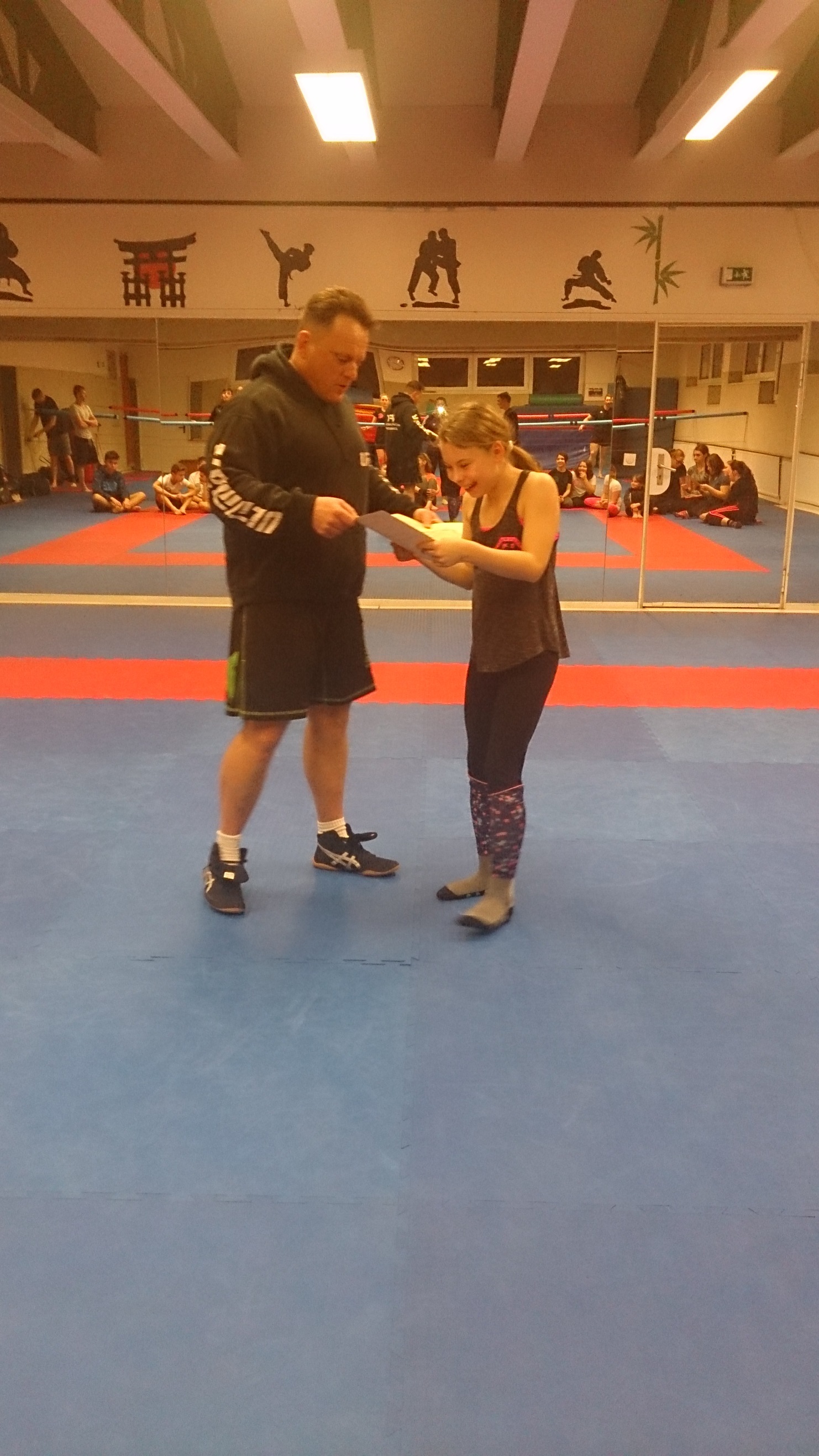 Trainer und Sportlerin stehen in einem Trainingsraum auf einer blauen Matte und besprechen eine Technik.