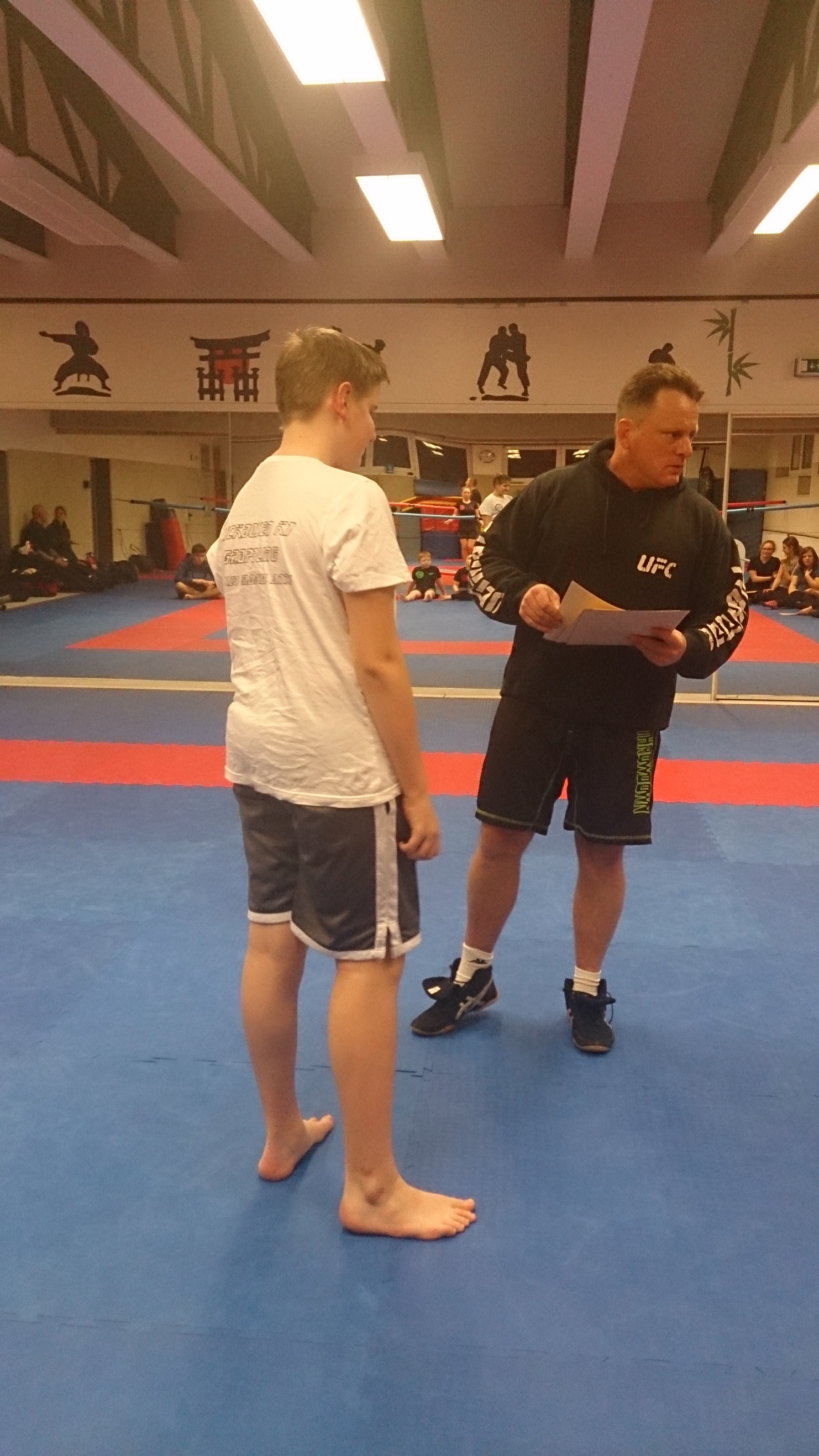 Trainingsszene in einem Kampfsportstudio mit einem Trainer und einem Sch&uuml;ler in Sportkleidung auf einer blauen Matte.