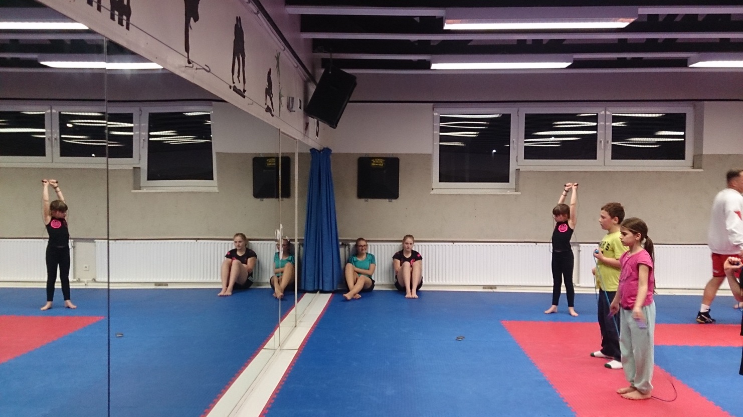 Gruppen von Kindern in einem Gymnastikraum, einige &uuml;ben vor einem Spiegel, andere sitzen auf der Matte.