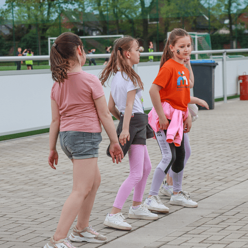 Drei Mädchen laufen auf einem gepflasterten Weg, während einer von ihnen ein oranges T-Shirt trägt und fröhlich aussieht.