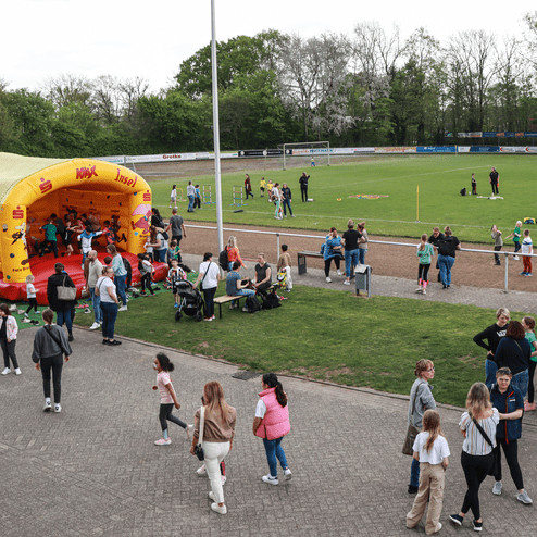 Familien und Kinder in einem Stadion, mit einer Hüpfburg und verschiedenen Aktivitäten auf dem Fußballfeld im Hintergrund.