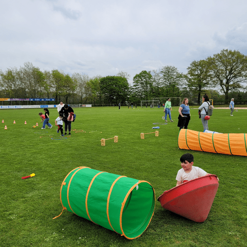 Kinder und Erwachsene spielen auf einem Rasenplatz mit bunten Hindernistunneln und Kegeln.
