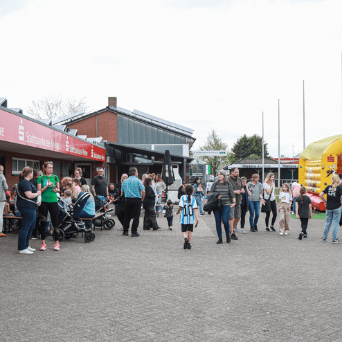 Menschenmenge vor einem Gebäude mit dem Schriftzug „Stadtsparkasse Rheinland“ und einem aufblasbaren Spielgerät.