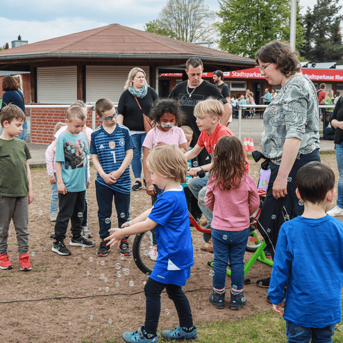 Gruppe von Kindern in einem Park, die um ein Fahrrad versammelt sind und Seifenblasen beobachten.