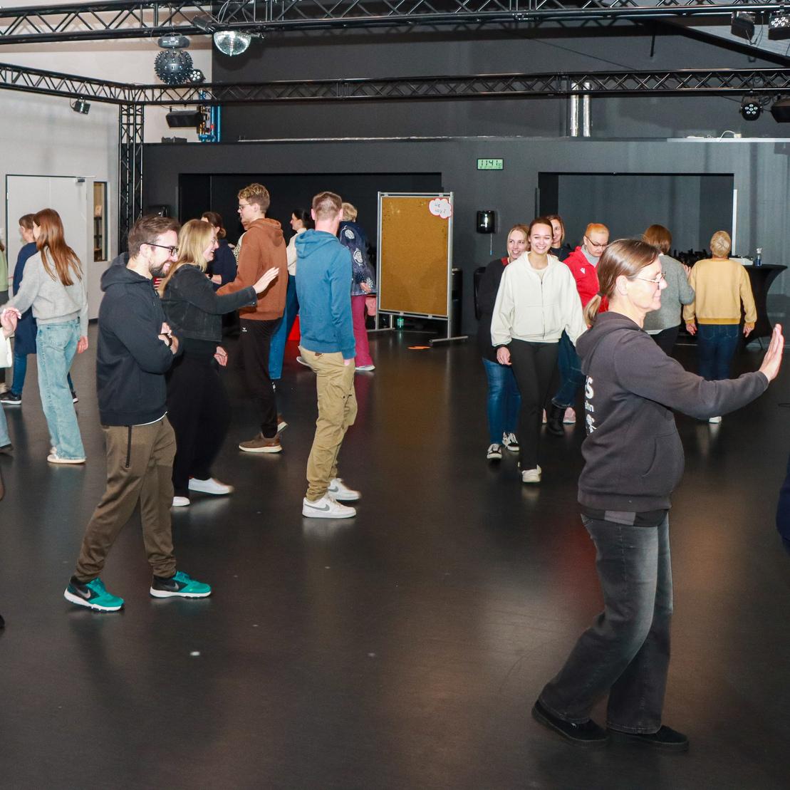 Eine Gruppe von Menschen tanzt in einem modernen Raum mit Spiegeln und B&uuml;hnenbeleuchtung.