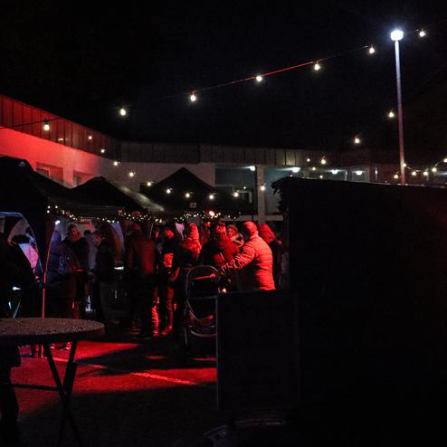 Nachtaufnahme einer Veranstaltung mit Menschen, Lichtern und Zelten in einer stimmungsvoll beleuchteten Umgebung.