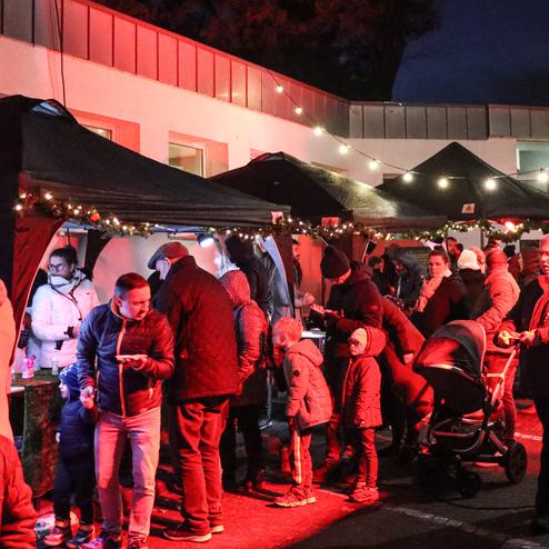 Belebter Weihnachtsmarkt mit Verkaufsst&auml;nden, Lichtern und Menschen, die gem&uuml;tlich zusammenstehen und sich unterhalten.