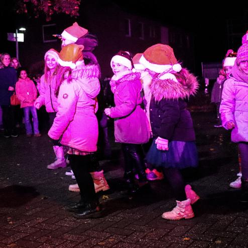 Gruppierung von Kindern in Weihnachtsm&uuml;tzen, die in der Dunkelheit fr&ouml;hlich zusammenstehen und tanzen.