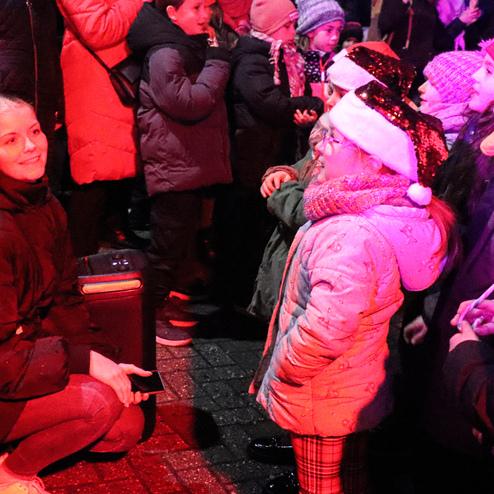 Zwei Erwachsene sprechen mit Kindern, die Weihnachtsm&uuml;tzen tragen, umgeben von einer festlichen Atmosph&auml;re.