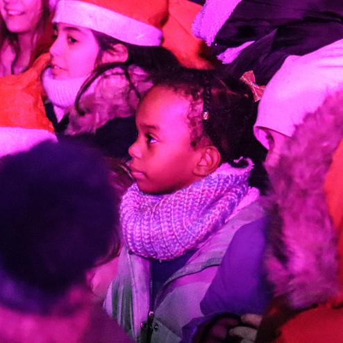 Gruppe von Kindern in Weihnachtsm&uuml;tzen, eines tr&auml;gt einen bunten Schal, bei Nacht in farbigem Licht.