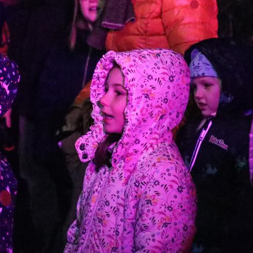 Bunte Kinder in Winterjacken freuen sich, w&auml;hrend sie in einem stimmungsvoll beleuchteten Umfeld stehen.