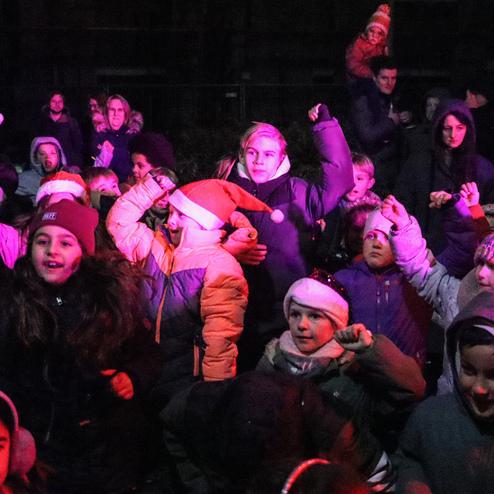Grupp von Kindern mit Weihnachtsm&uuml;tzen feiert fr&ouml;hlich bei einer Veranstaltung in dunkler Umgebung.