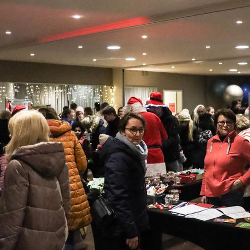 Menschenmenge in festlicher Atmosph&auml;re, einige tragen Weihnachtsm&uuml;tzen, bei einem Markt mit St&auml;nden und Dekoration.