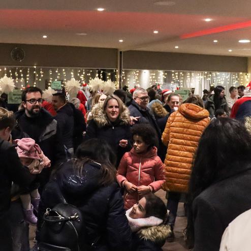 Menschenmenge in festlicher Atmosph&auml;re, mit Weihnachtsdekoration und Gruppen, die miteinander interagieren.