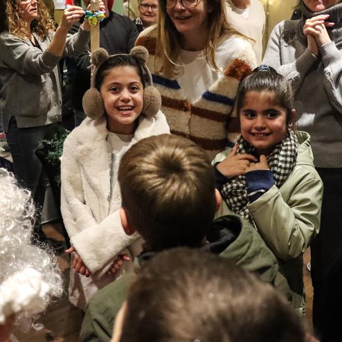 L&auml;chelnde Kinder stehen in einer Gruppe, umgeben von Erwachsenen, w&auml;hrend Weihnachtsmann in der N&auml;he ist.