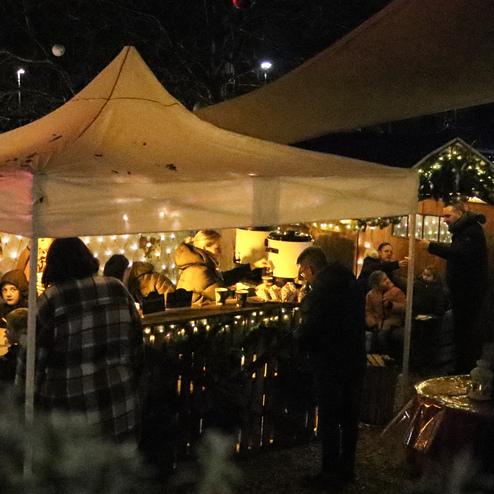 Beleuchtetes Festzelt mit Menschen, die Getr&auml;nke genie&szlig;en, umgeben von weihnachtlicher Dekoration und stimmungsvollem Licht.