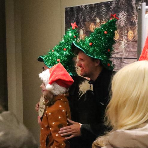 Mann und Kind in Weihnachtsm&uuml;tzen posieren l&auml;chelnd vor einer festlich dekorierten Wand.