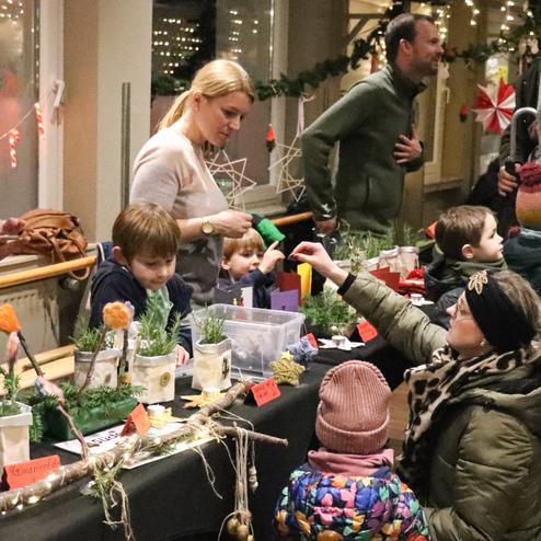 Menschen stehen an einem Verkaufstisch mit Pflanzen, w&auml;hrend Kinder und Erwachsene miteinander interagieren.