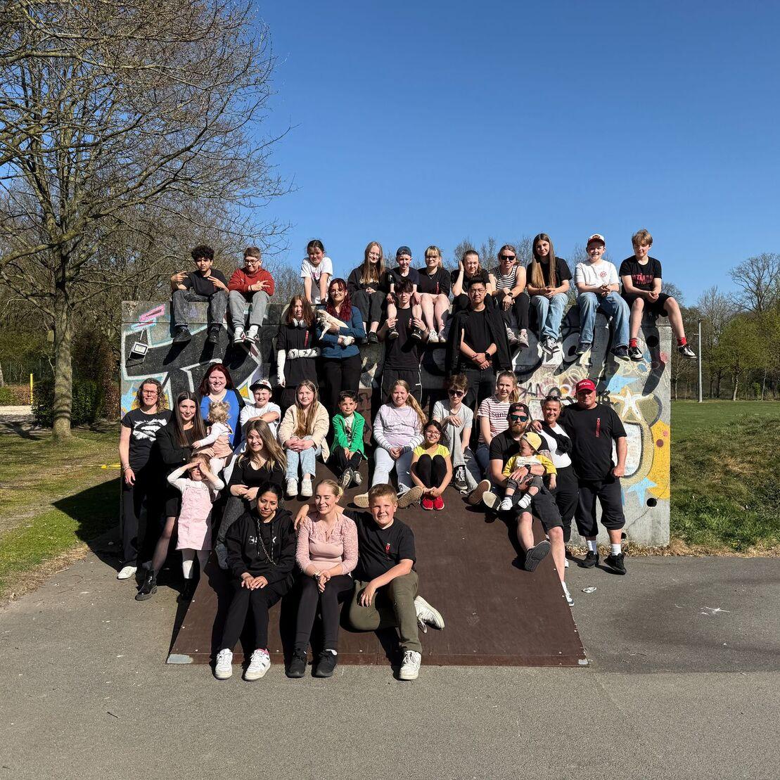 Gruppendfoto von rund 40 Personen auf einer Skateboardrampe in einem Park an einem sonnigen Tag.