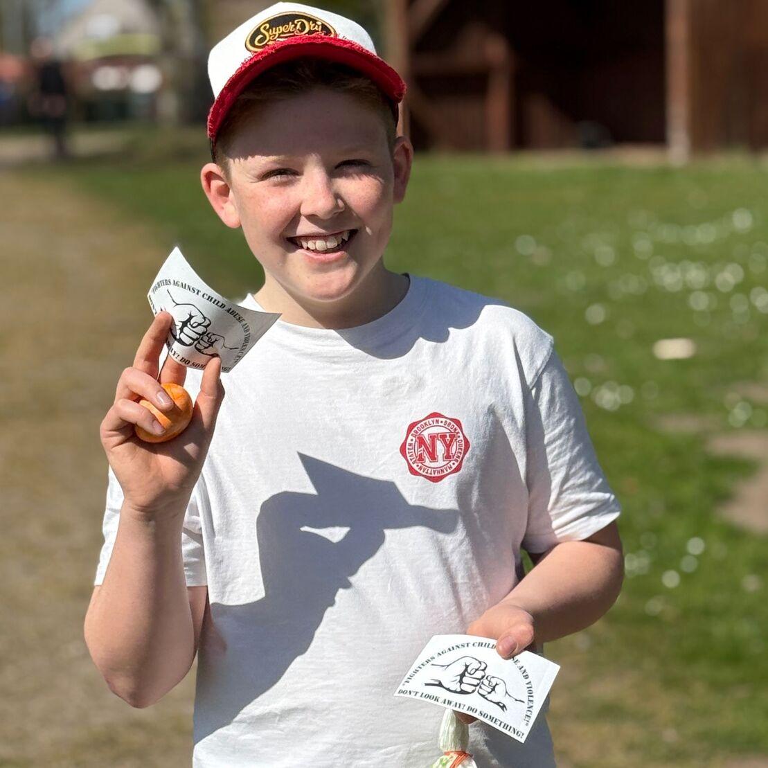 Junge mit einem lachenden Gesicht, h&auml;lt in jeder Hand eine T&uuml;te mit Snacks, im freudigen Ambiente eines Parks.