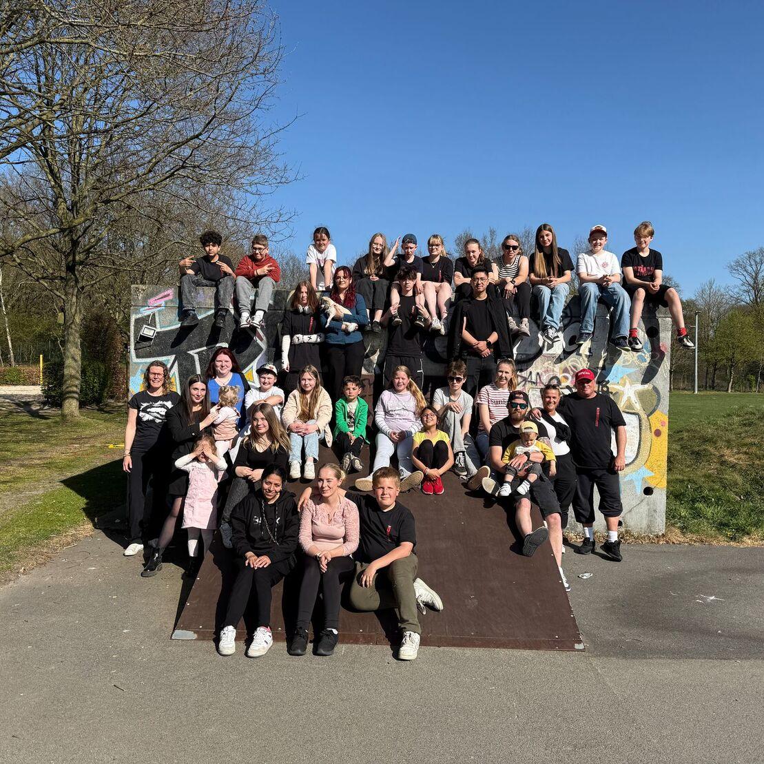 Gruppenfoto von &uuml;ber 40 Jugendlichen, die auf einer Rampe in einem Park im Freien posieren, bei sonnigem Wetter.