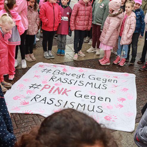 Gruppierung von Kindern und Erwachsenen in Pink, um ein Banner mit den Aufschriften &bdquo;#Bewegt Gegen RASSISMUS&ldquo; und &bdquo;#PINK Gegen RASSISMUS&ldquo; zu pr&auml;sentieren.